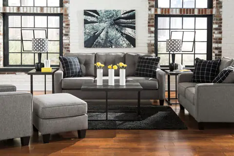 Grey fabric sofa, loveseat and ottoman with patterned cushions against industrial windows