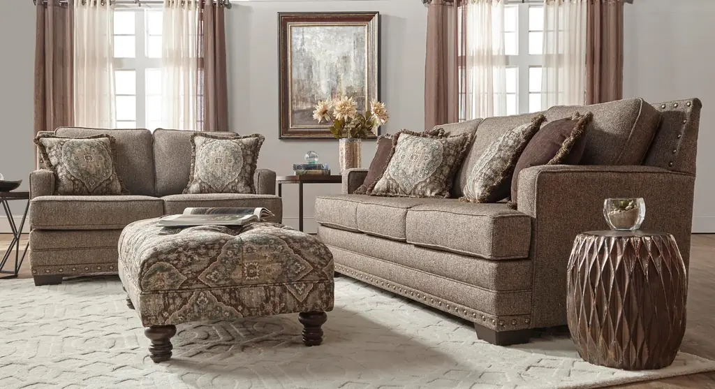 Upholstered nailhead sofa and loveseat with a patterned ottoman in a staged room